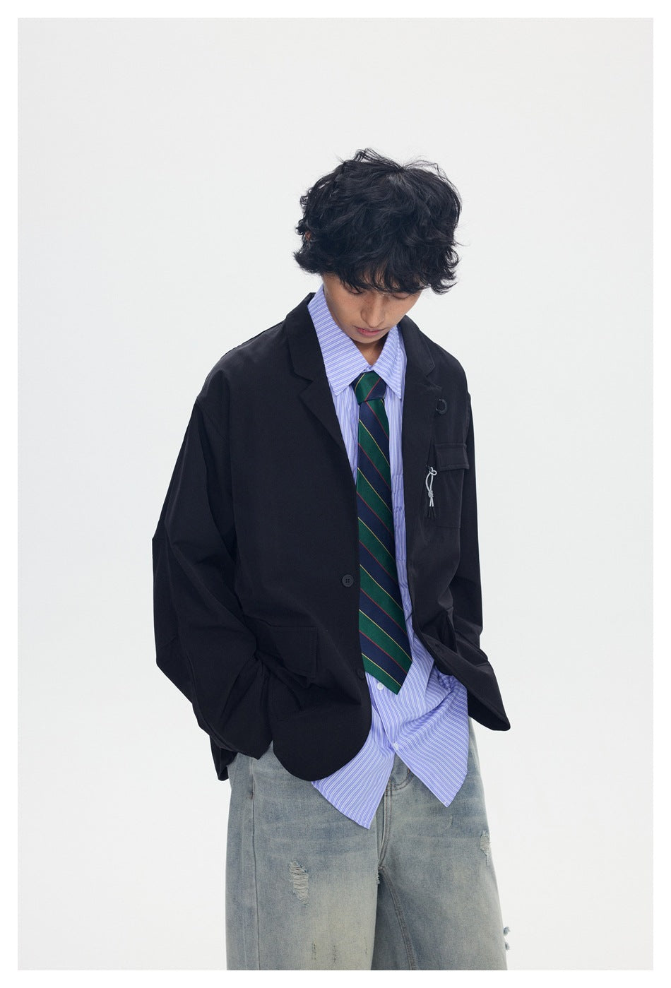 Model wearing an oversized black blazer with flap and zip chest pockets, a striped shirt, tie, and loose jeans.