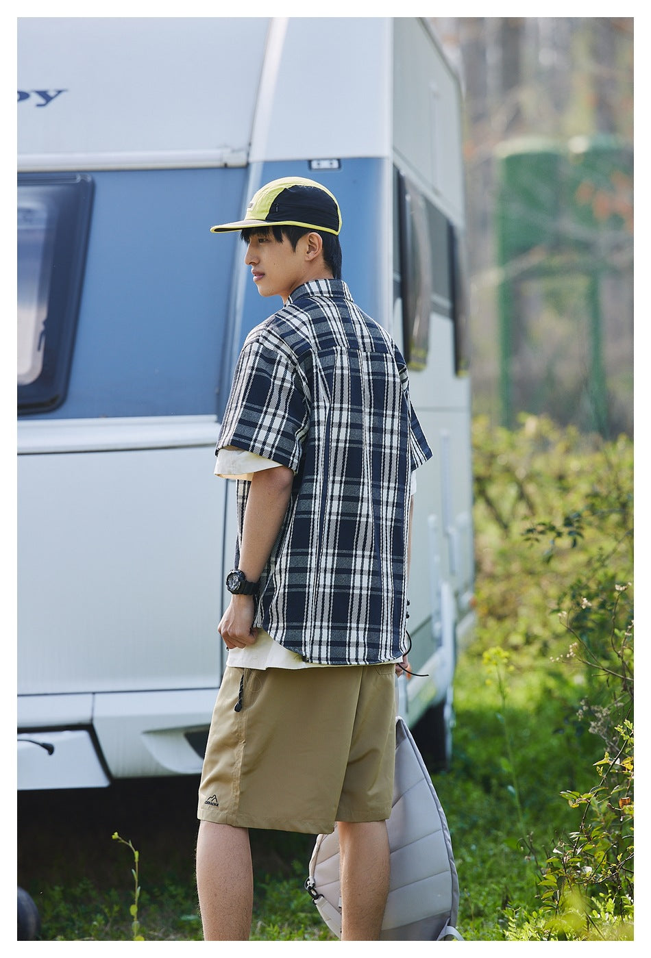 Rear three-quarter view of a model wearing a navy and white plaid short-sleeve shirt and khaki shorts.