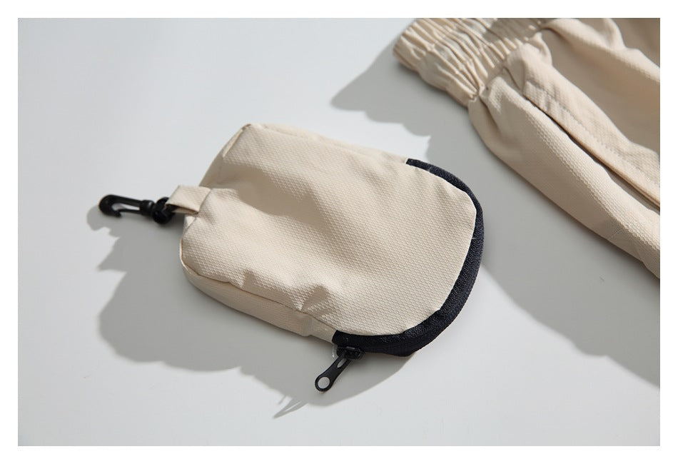 Cream fabric pouch with dark trim and zipper beside a gathered pant leg.