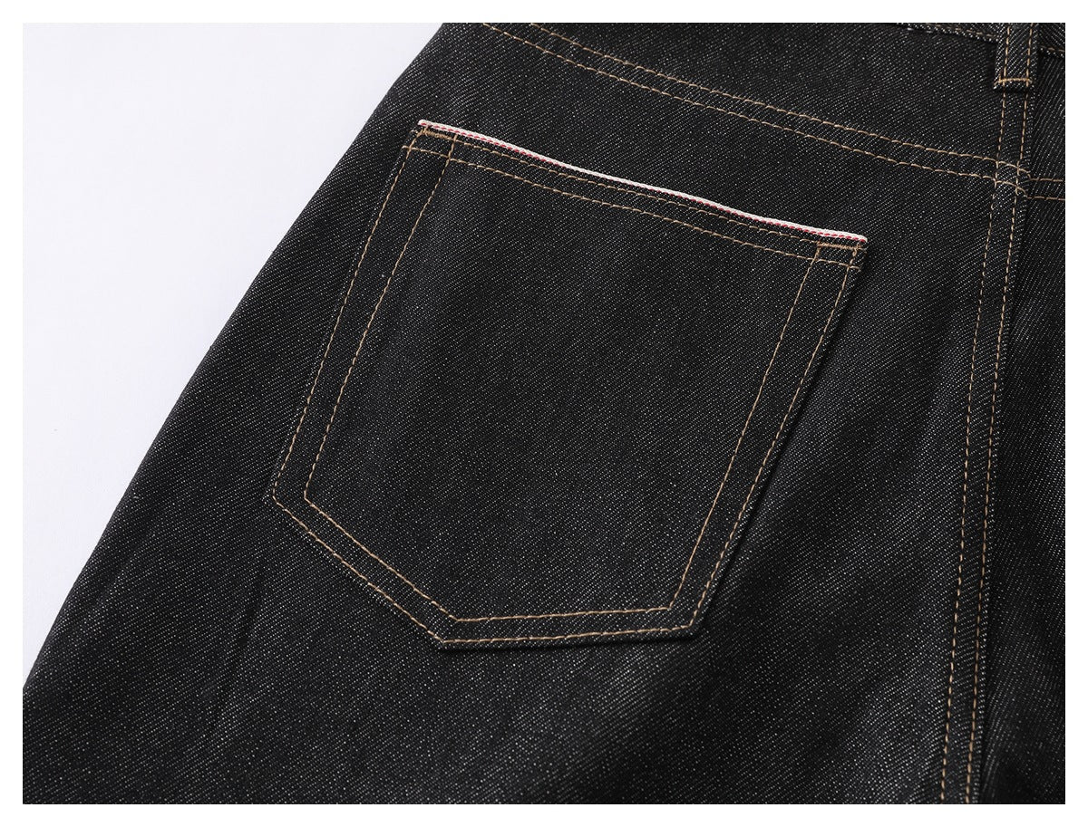 Close-up of one rear patch pocket on black denim jeans with tan stitching and a narrow red-and-white trim.