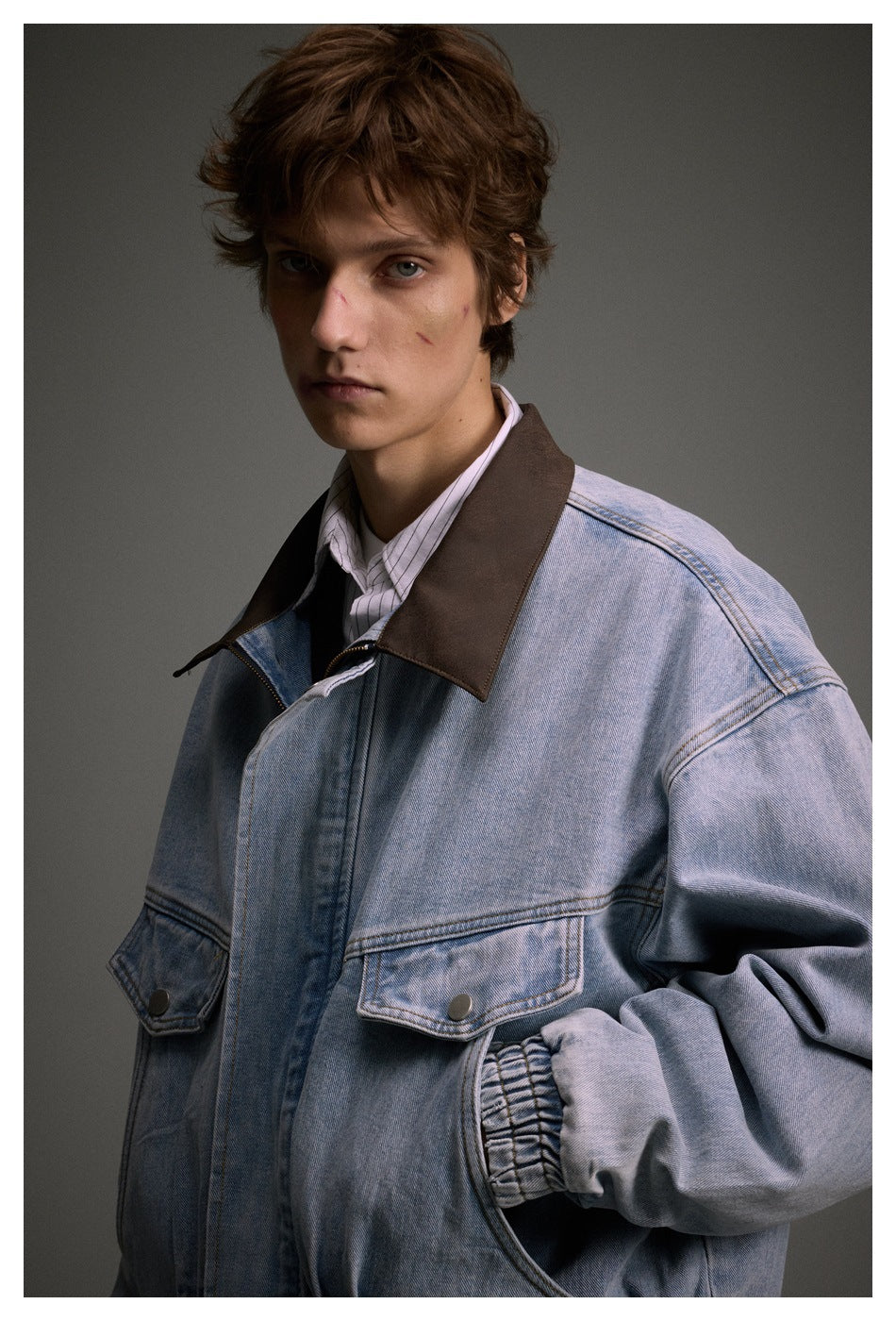 Close view of a model wearing a light blue denim jacket with a dark brown collar and snap-flap chest pockets.