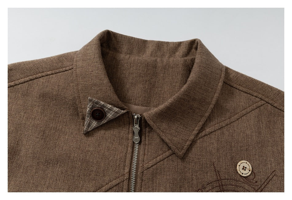 Close-up of the brown jacket’s collar, zipper, plaid under-collar accent, and decorative stitching.