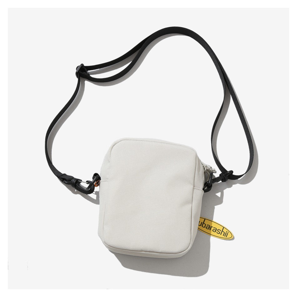 Back view of an off-white crossbody bag with a plain panel, black adjustable strap, and attached yellow tag.