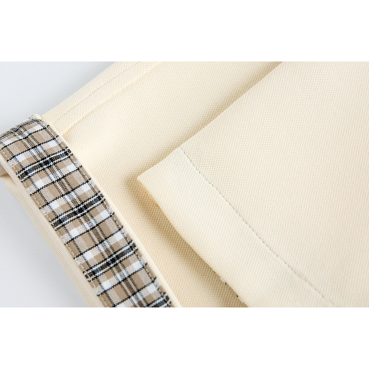 Close-up of a cream shirt with tan plaid trim beside a stitched fabric panel.