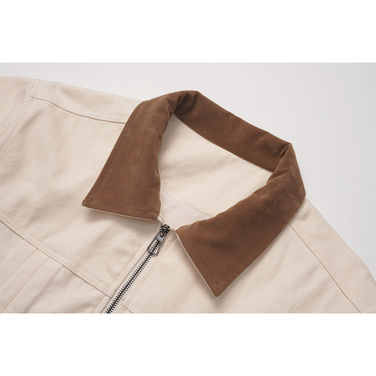 Close-up of a cream jacket with a brown pointed collar and silver front zipper.