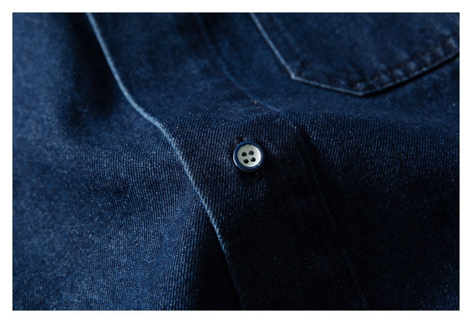 Close-up of a light four-hole button and stitching on dark blue denim fabric.