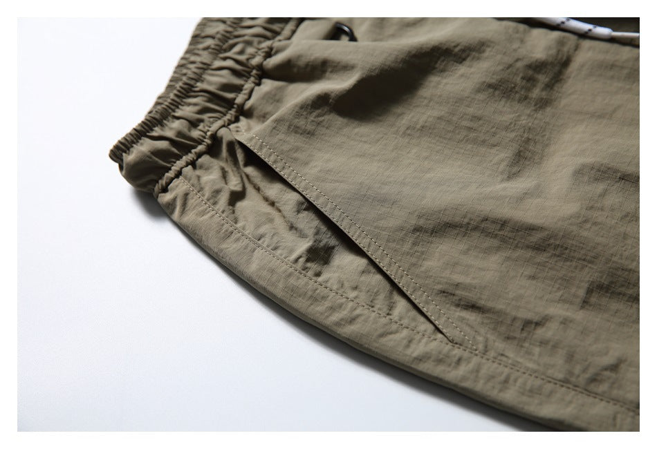 Close-up of olive-khaki shorts showing the elastic waistband, angled pocket opening, and stitched hem.