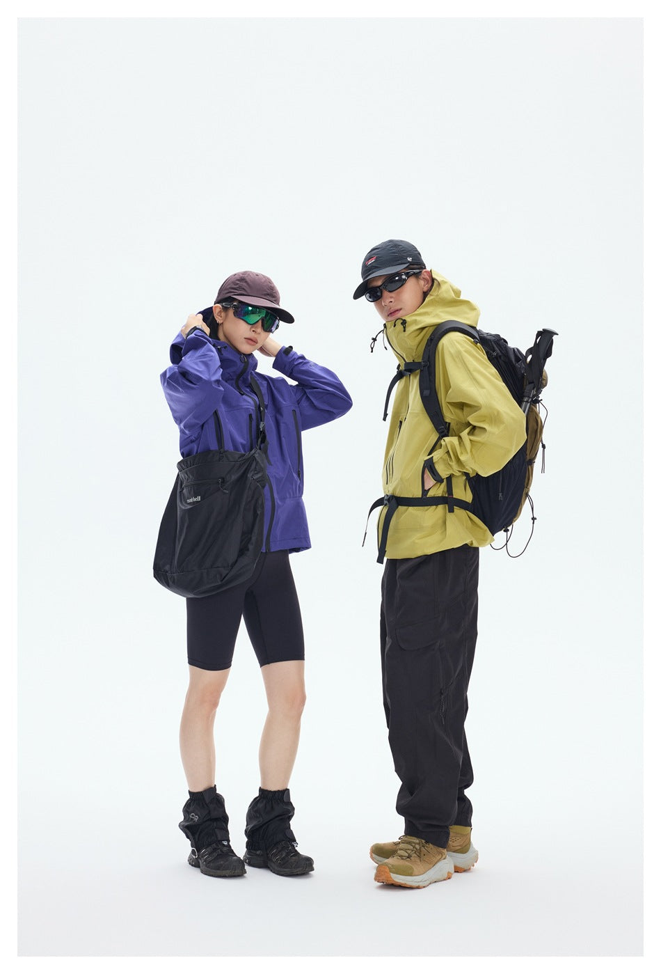 Two hikers pose in purple and yellow jackets; the yellow-jacketed hiker carries a large brown backpack.