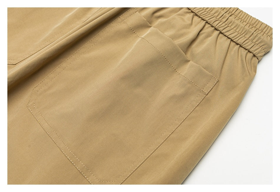 Close-up of a large stitched patch pocket on tan pants near the elastic waistband.