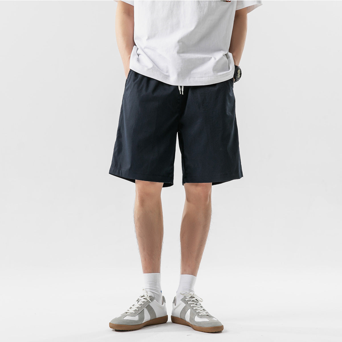 Cropped model wearing dark navy drawstring shorts with a white T-shirt and sneakers, front view.
