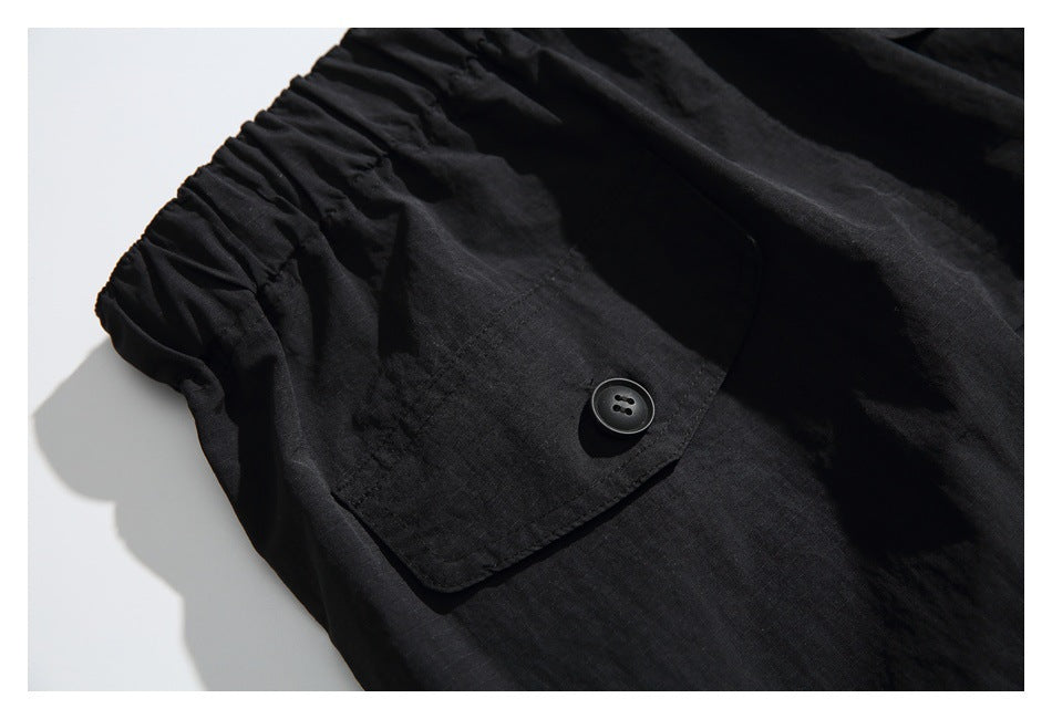 Close-up of black pants showing a gathered waistband and a flap pocket with a black button.