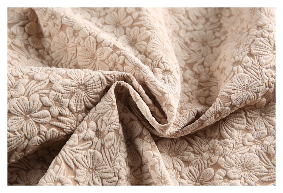 Close-up of beige raised floral fabric arranged in soft folds.