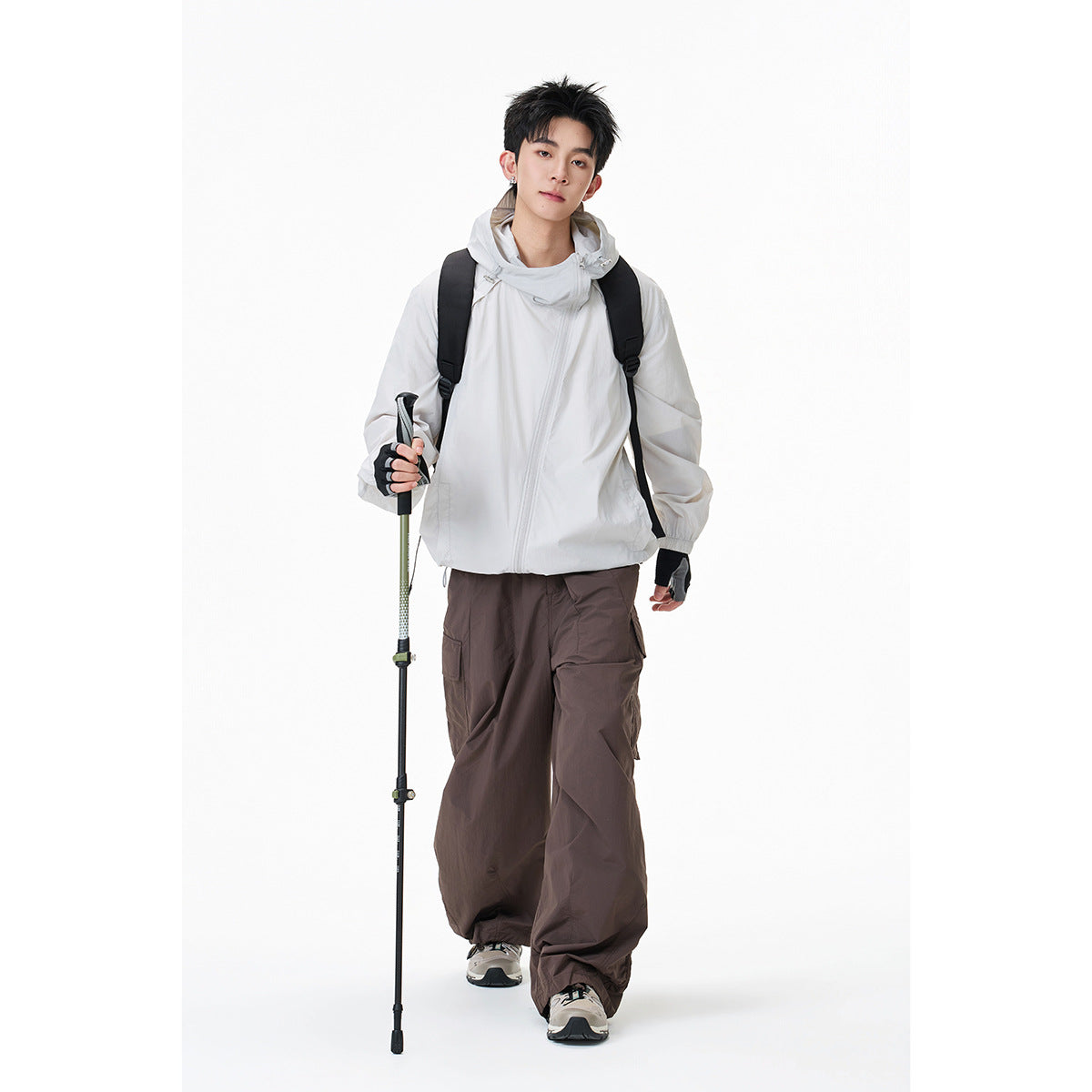 Model wearing a white hooded windbreaker with dark brown cargo trousers and a backpack.