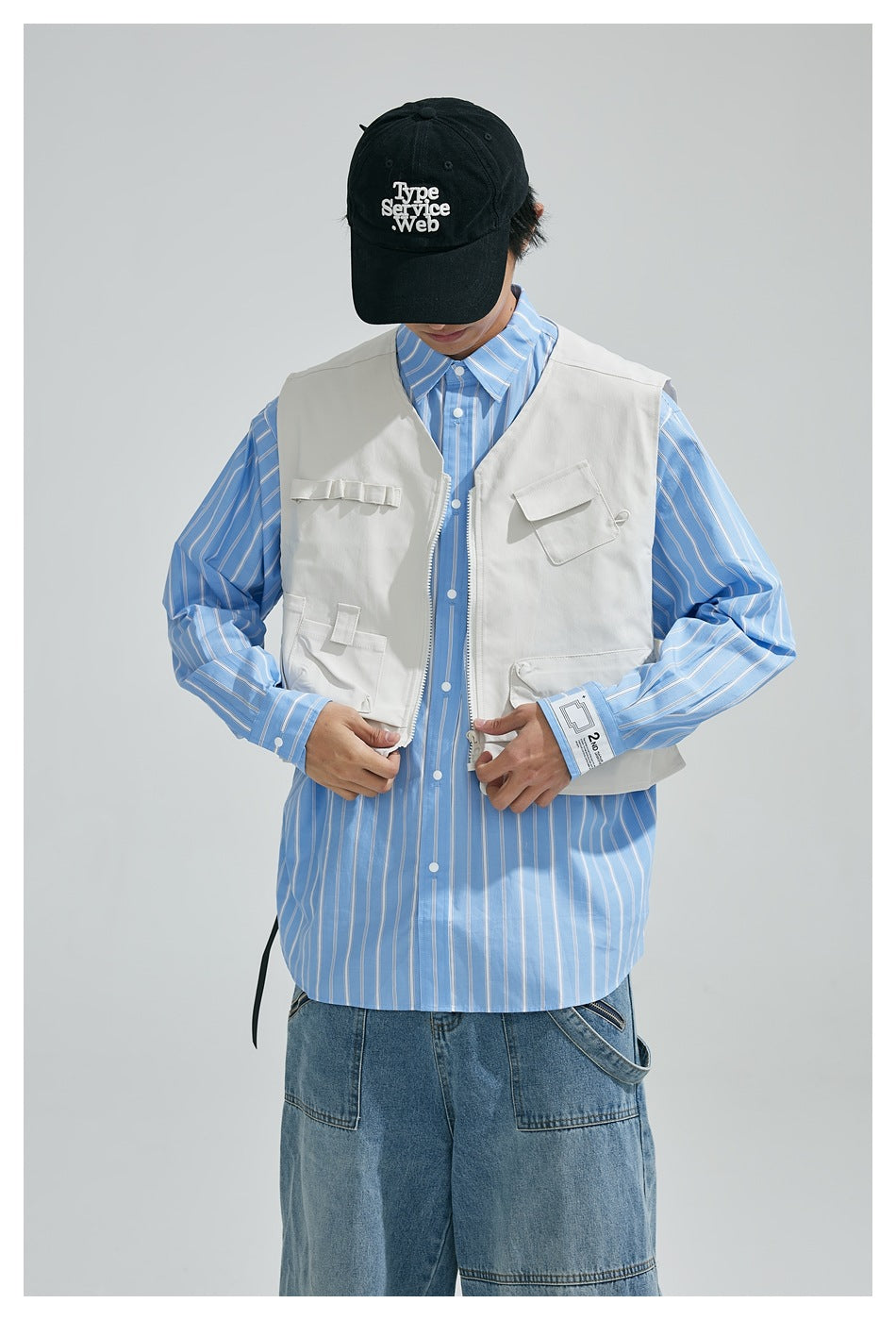 Model adjusts a white multi-pocket utility vest worn over a blue striped shirt.