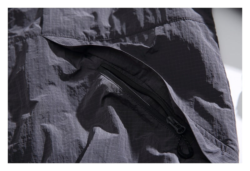Close-up of a black zip pocket beneath a flap on charcoal gray ripstop fabric.