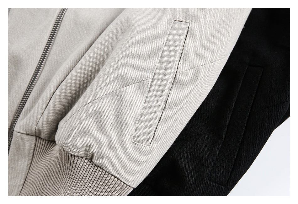 Close-up of zip and welt pocket details on light beige and black jacket fabric.