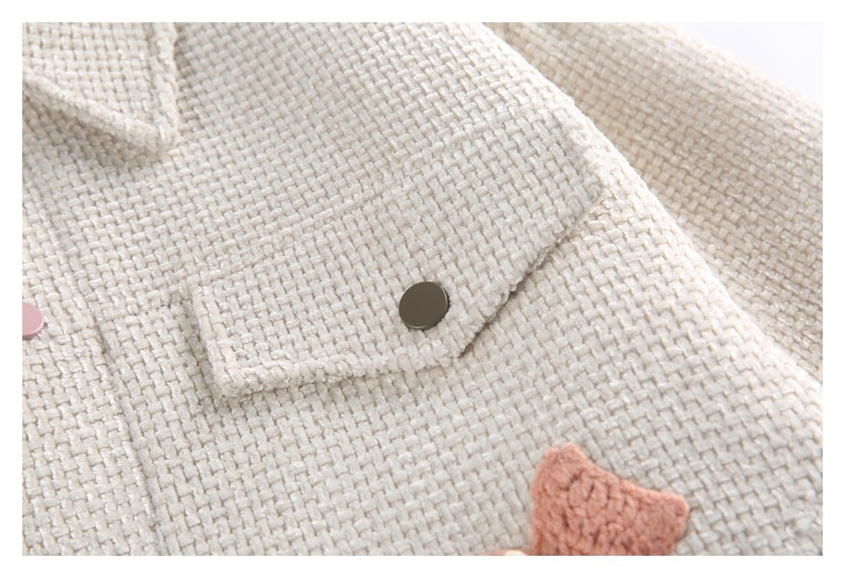 Close-up of an ivory textured jacket with a flap and dark snap, plus partial pink appliqué.