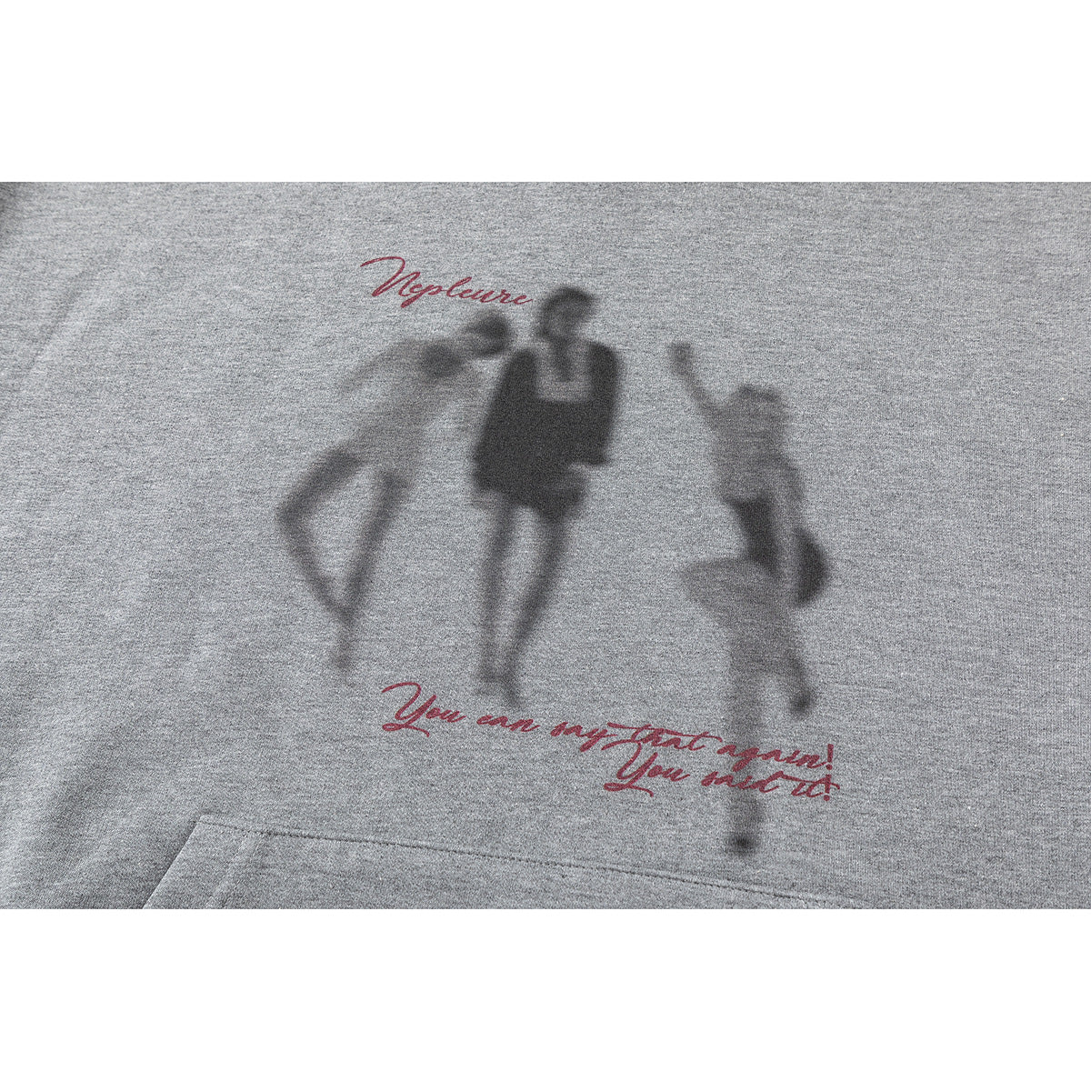 Close-up of a gray hoodie’s front graphic, with blurred figures and red cursive lettering above a kangaroo pocket.
