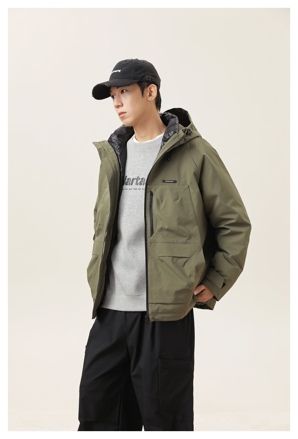 Model wearing open army green hooded jacket with black puffer inner collar over a gray sweatshirt and black pants