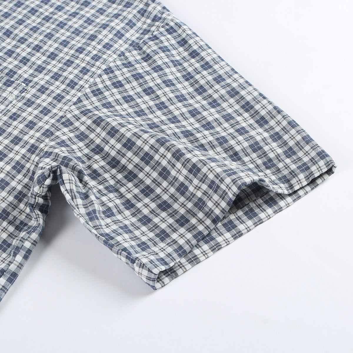 Close-up of the short sleeve and stitched hem on a blue-gray and white plaid shirt.