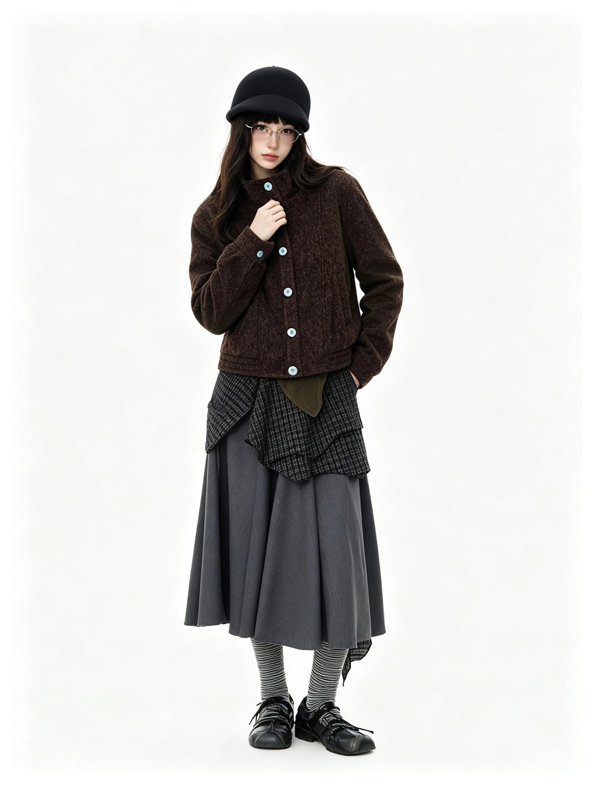 Model wearing a brown cropped button-up jacket with a gray layered midi skirt, black cap and striped socks