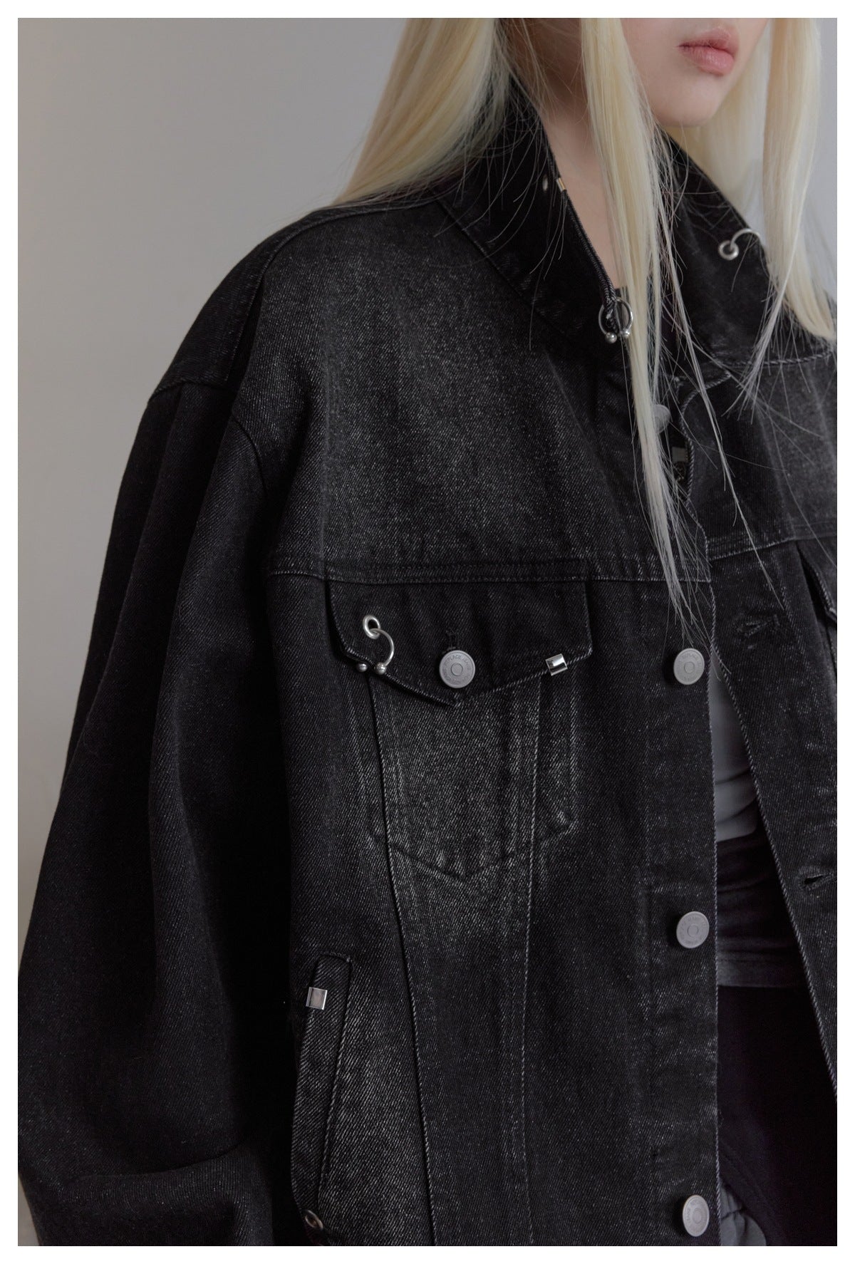 Close view of a black denim jacket's front pocket, seams, metal buttons, and decorative silver hardware.