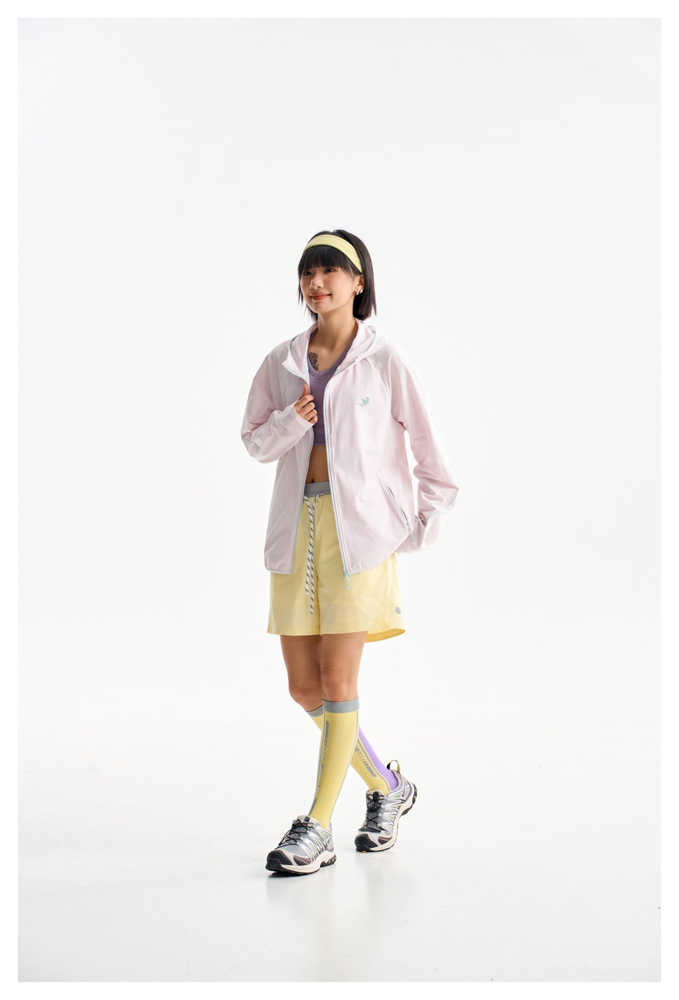 Model wearing an open pale pink hooded jacket with yellow shorts and a lavender top.