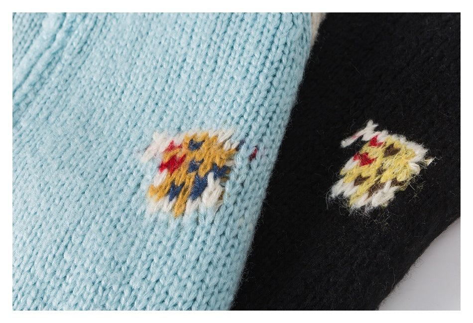 Close-up of aqua and black knit fabric, each with a small multicolor embroidered motif.
