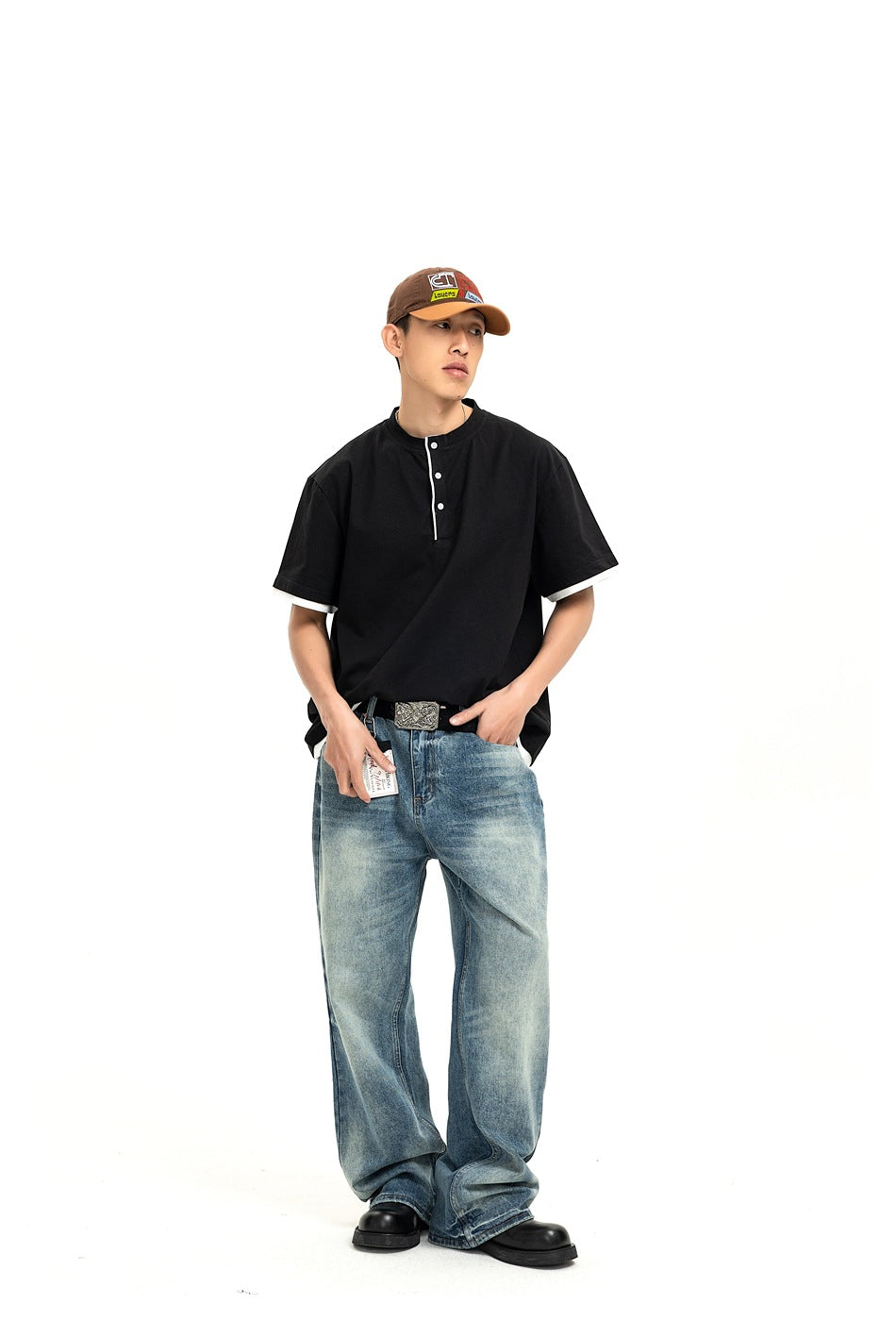 Model in a black Henley shirt with white sleeve trim and loose blue jeans, standing at a slight angle.
