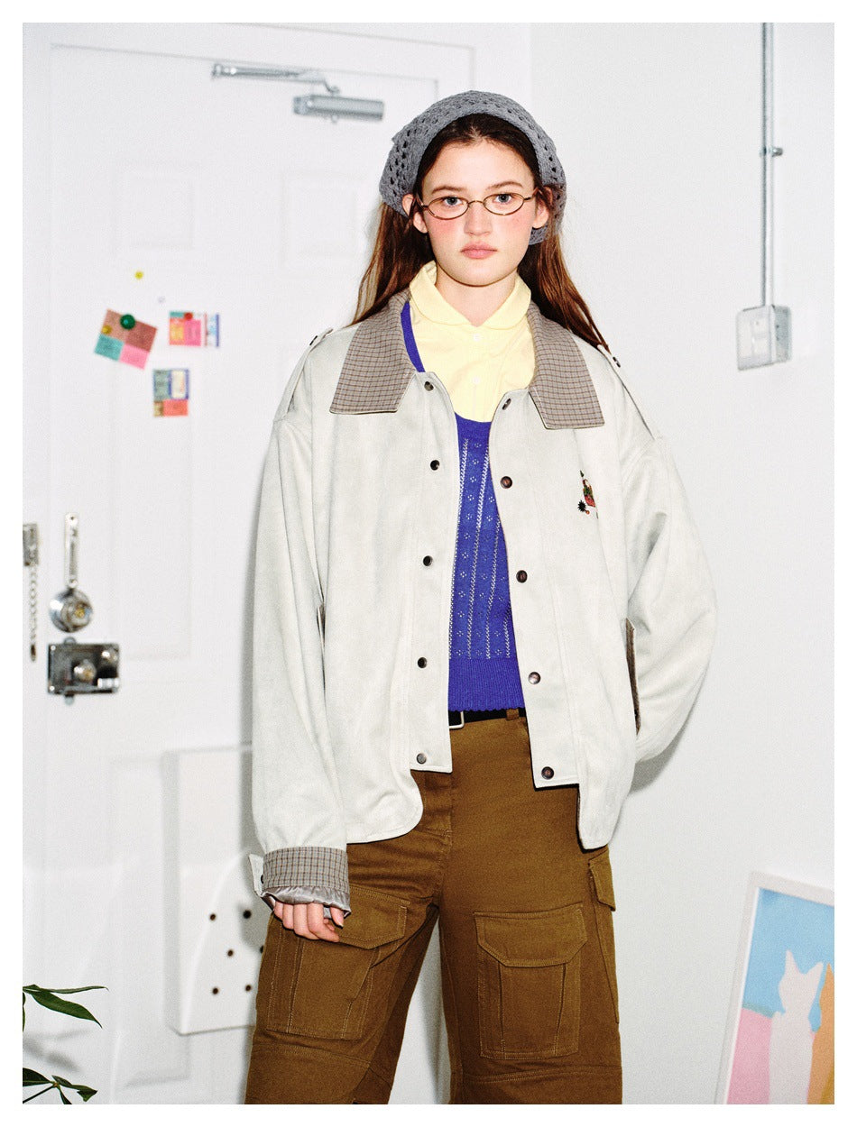 Close view of a model wearing a pale gray jacket with checked collar and cuffs over a blue sweater and yellow shirt.