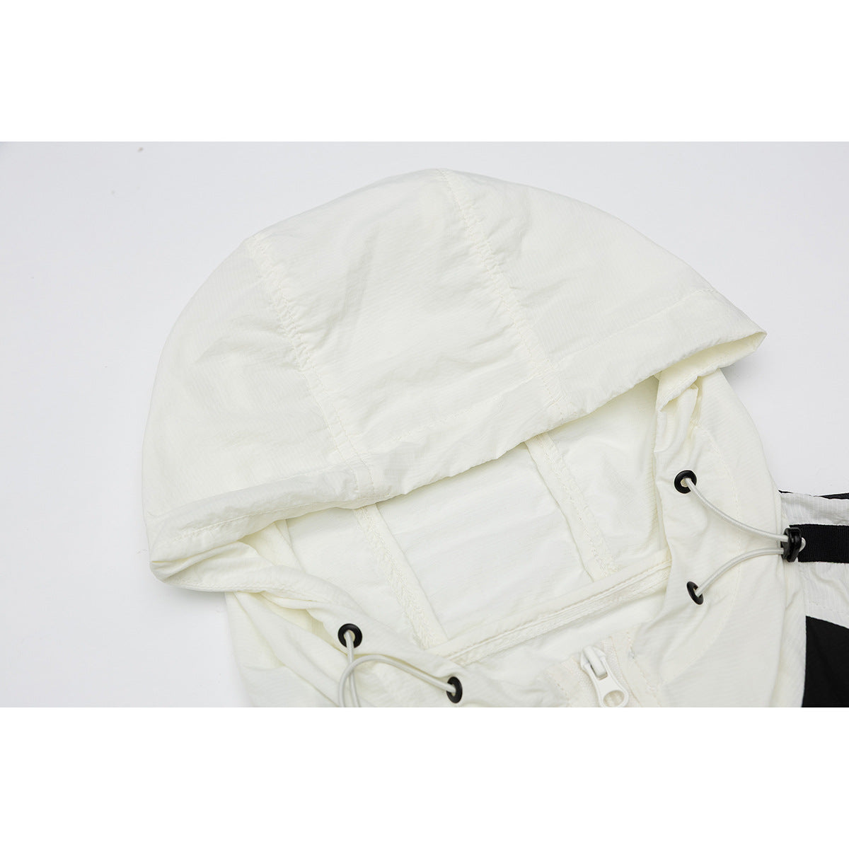 Close-up of an ivory jacket hood with panel seams, drawcord eyelets and a light-colored zipper.