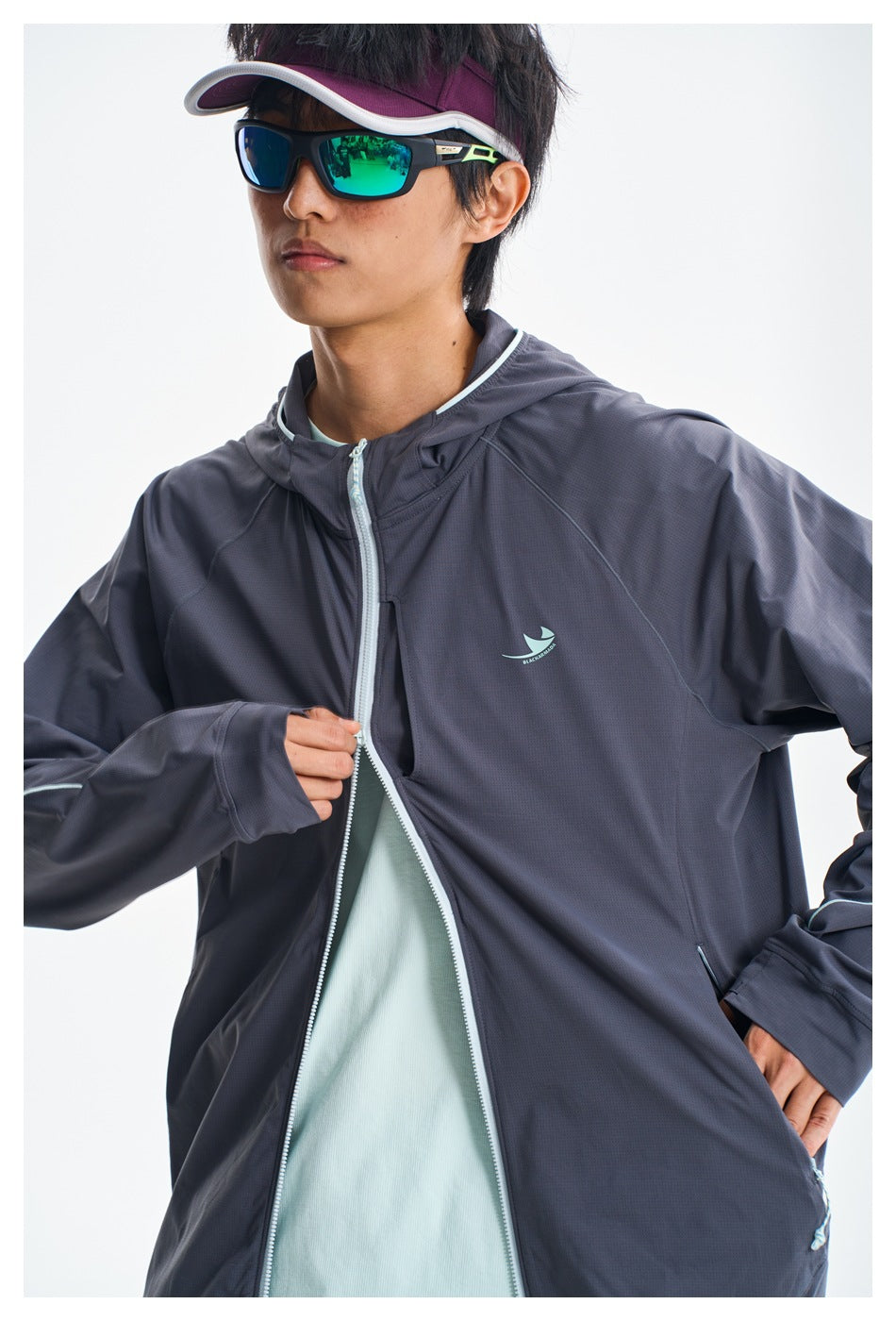 Close-up of a model wearing a charcoal hooded jacket with pale aqua zipper trim and a small chest emblem.