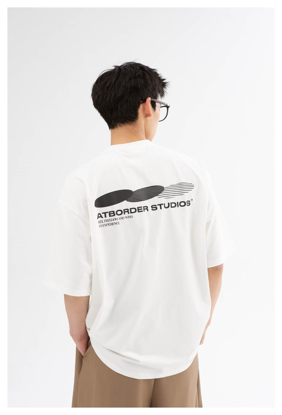 Model viewed from behind wearing an oversized white T-shirt with a large black graphic and English text on the back.