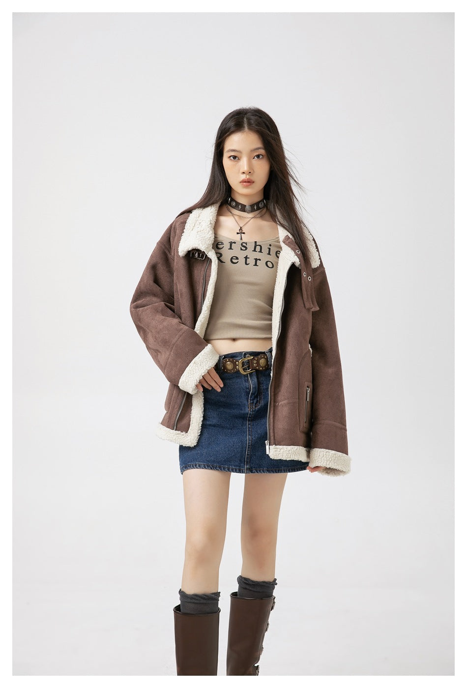 Model wearing an open brown fleece-trimmed jacket over a beige graphic top and blue denim skirt.