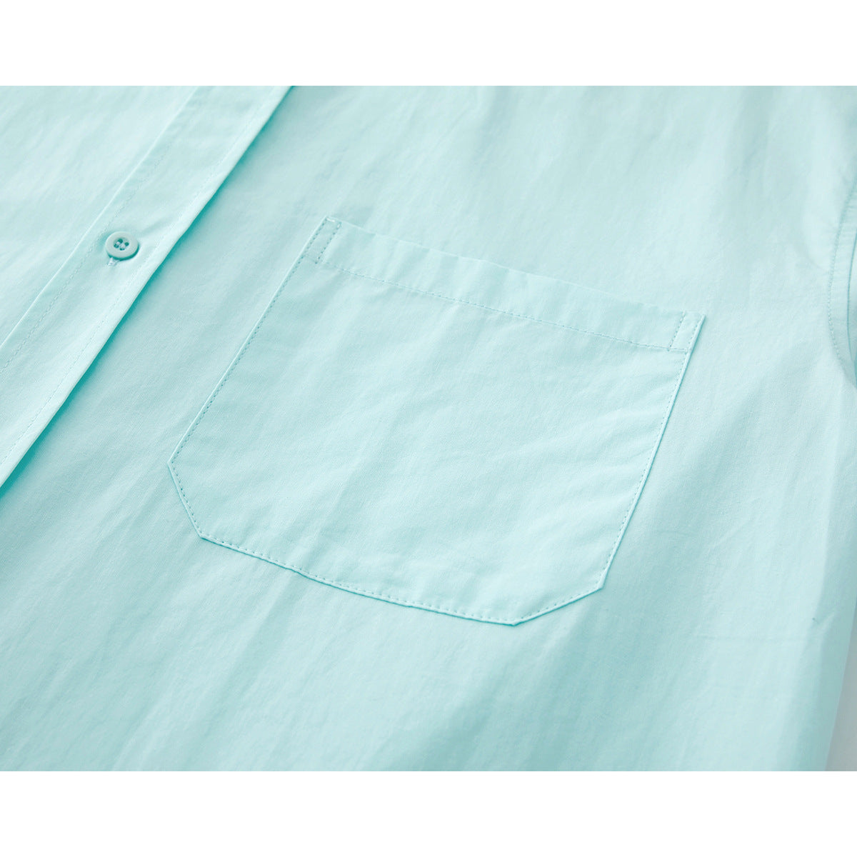 Close-up of a pale aqua shirt's stitched chest pocket and button placket.