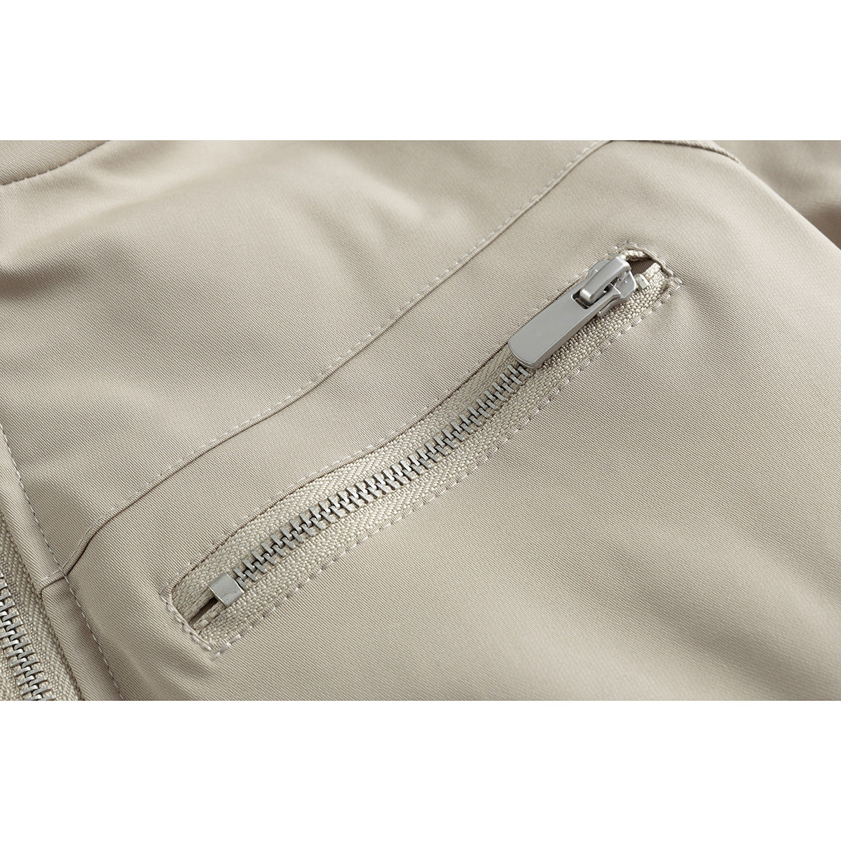 Close-up of a beige jacket's slanted zip pocket with a silver zipper pull.