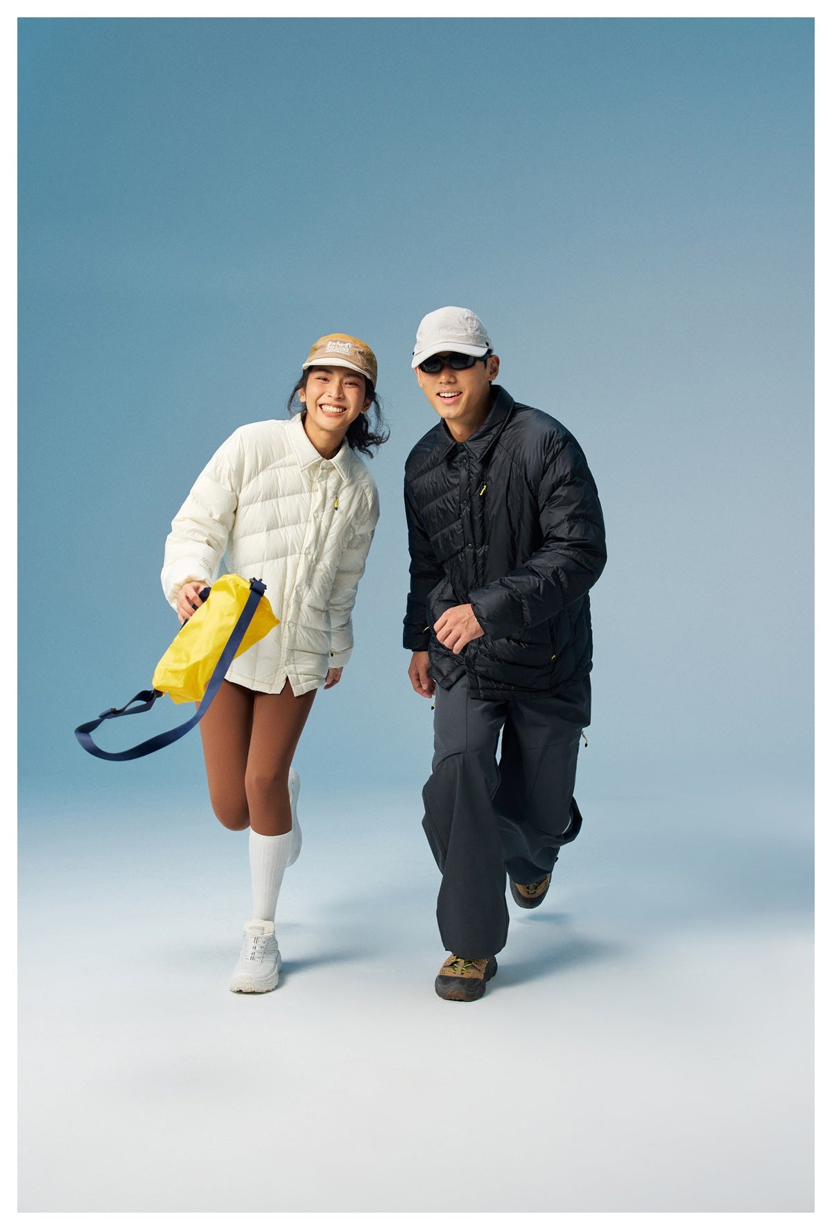 Two models pose in cream and black puffer jackets, with a bright yellow bag in the foreground.