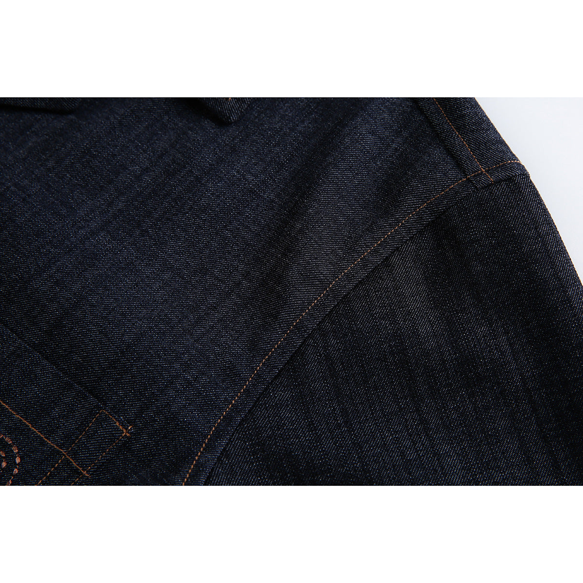 Close-up of dark indigo denim fabric and a curved seam with orange topstitching.