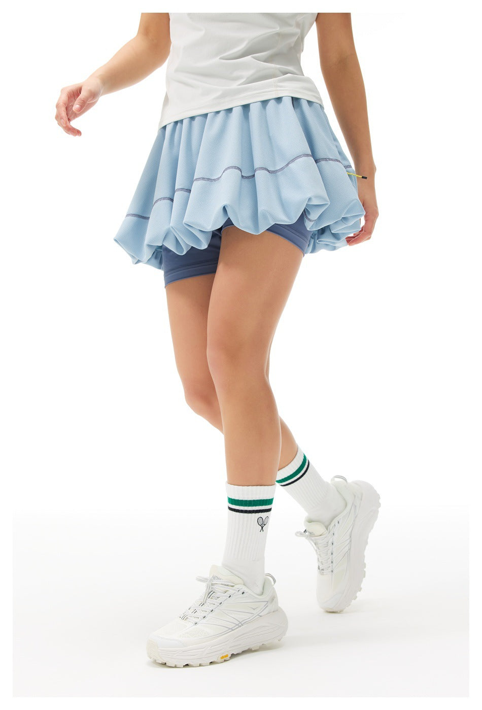 Angled rear view of a model wearing a light blue bubble tennis skirt with dark blue built-in shorts.