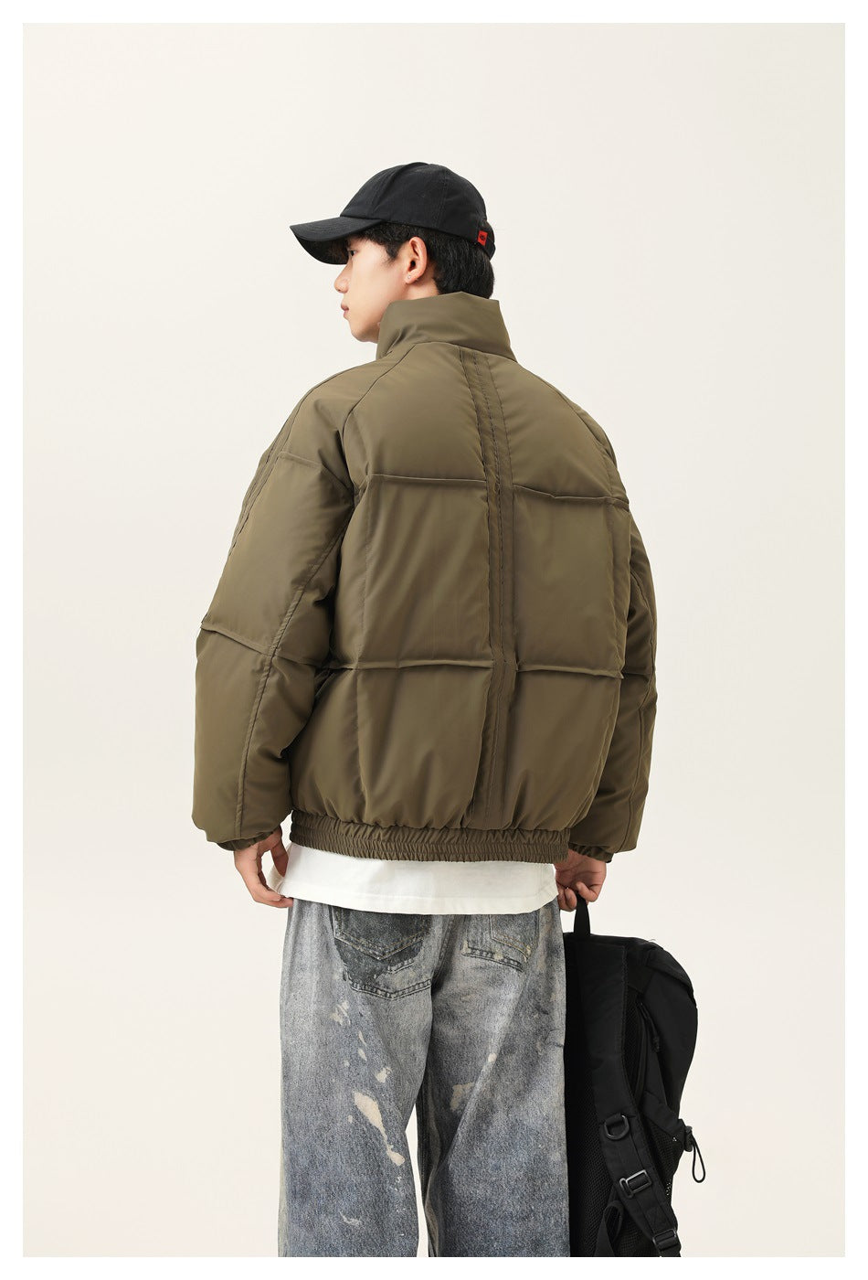 Back view of a model wearing an olive green padded jacket with panel seams and an elastic hem.