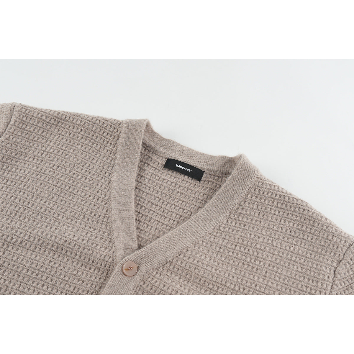 Close-up of a taupe textured cardigan showing its V-neck, button, and sewn neck label.