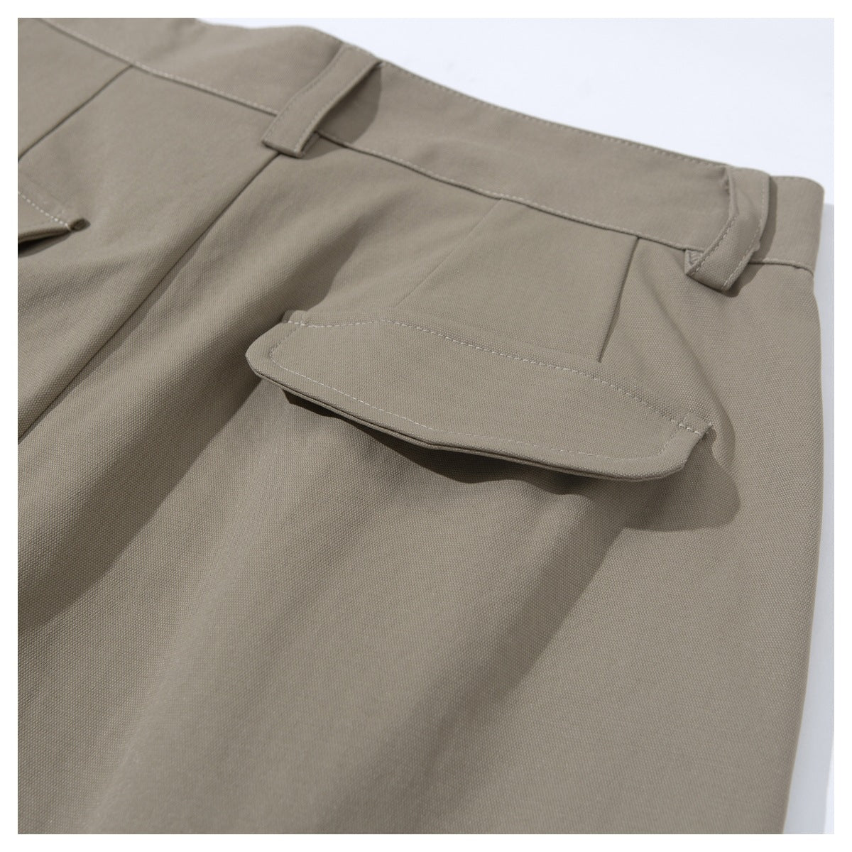 Close-up of taupe trousers showing the waistband, belt loops, and a flap pocket.
