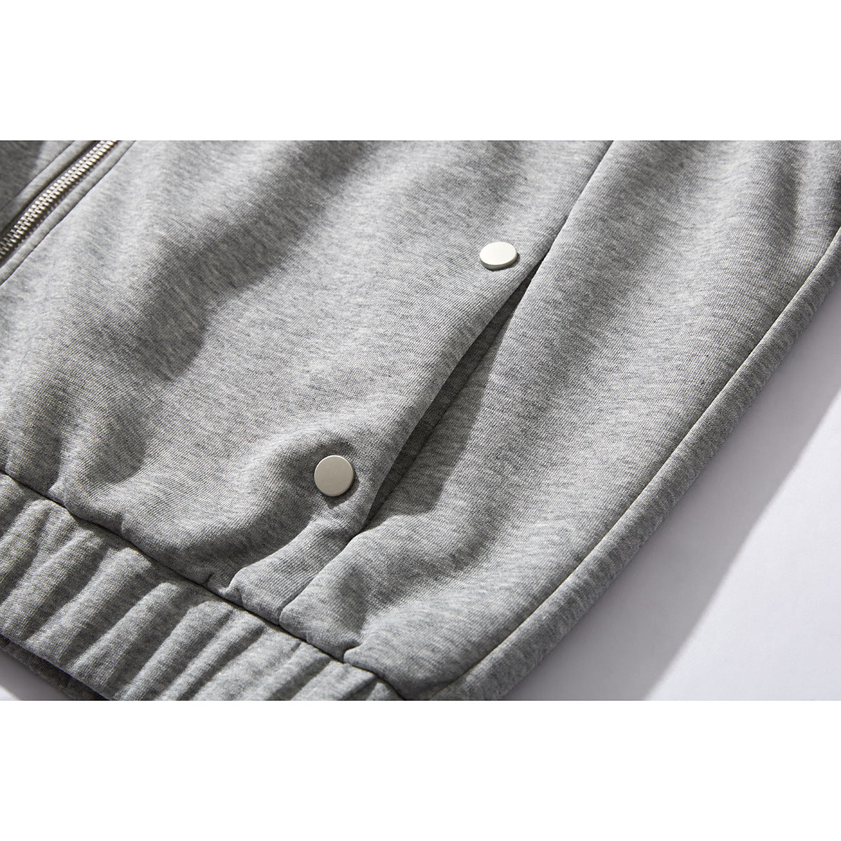 Close-up of a gray jacket's lower front with snap buttons, hem, and part of the zipper.