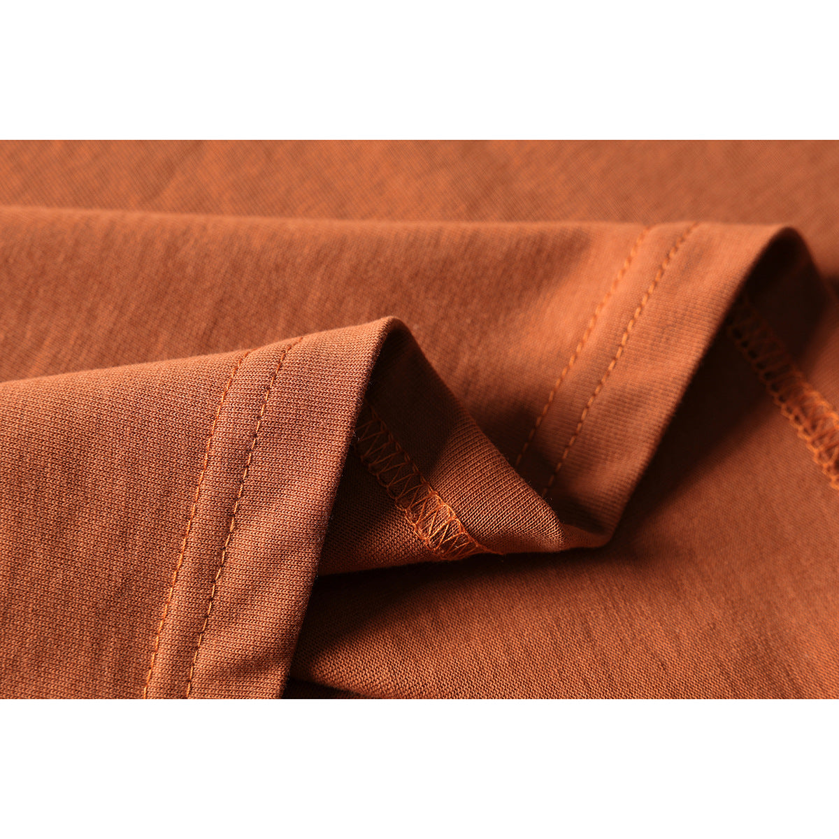 Close-up of rust-orange T-shirt fabric folded to show the stitched hem and inner overlock seam.