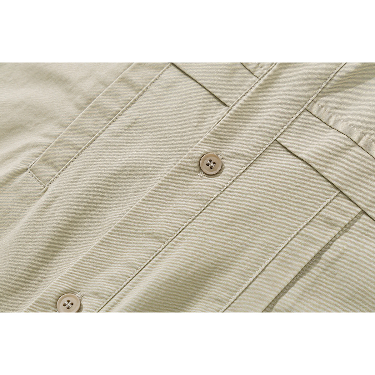 Close-up of light beige shirt fabric, stitching, and two buttons on the placket.