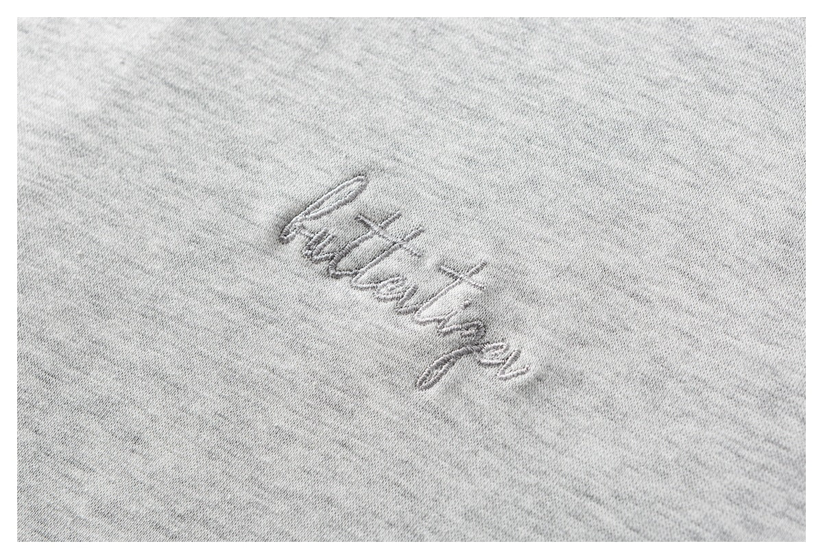 Close-up of small gray cursive embroidery on light gray heathered fabric.