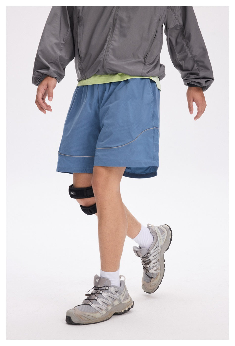 Angled front view of a person wearing blue athletic shorts with curved contrast piping and a wide hem.
