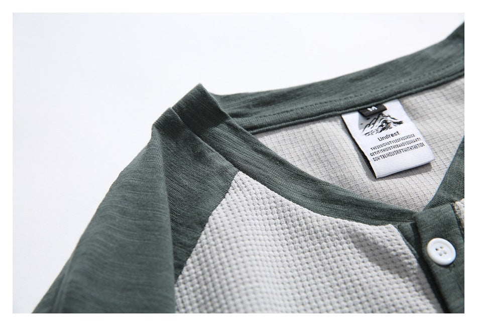 Close-up of a light gray waffle-knit shirt with dark green collar and shoulder panels, a white button, and a neck label.