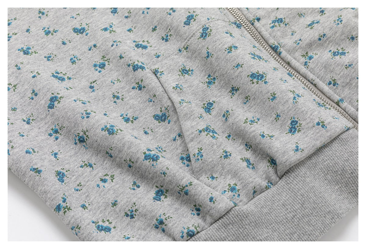 Close-up of a gray floral hoodie showing its zipper, pocket seam, and ribbed hem.