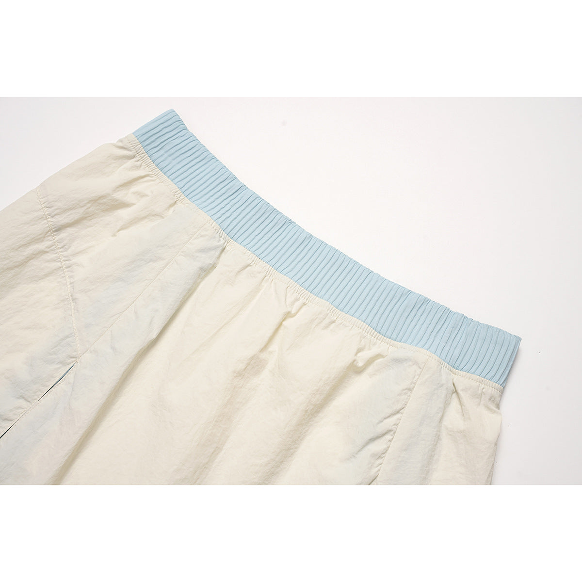 Close-up of an ivory skirt with a wide light-blue ribbed elastic waistband and stitched panel seams.